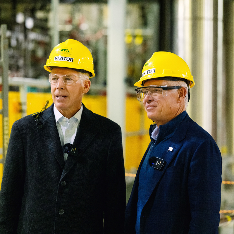 Two professionals standing in a laboratory building wearing yellow hard hats