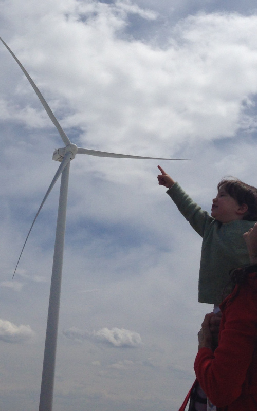 A NREL employee's daughter points at the turbines while in her mother's arms at the National Wind Technology Center.