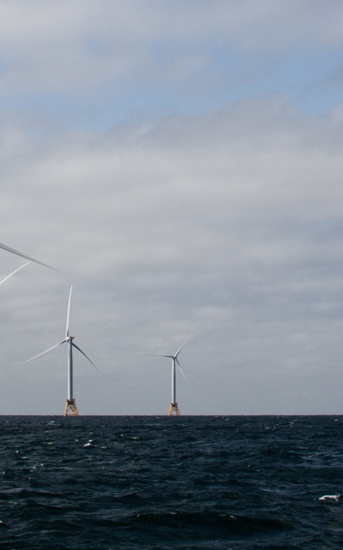 Offshore wind turbines at sea with sun shining.