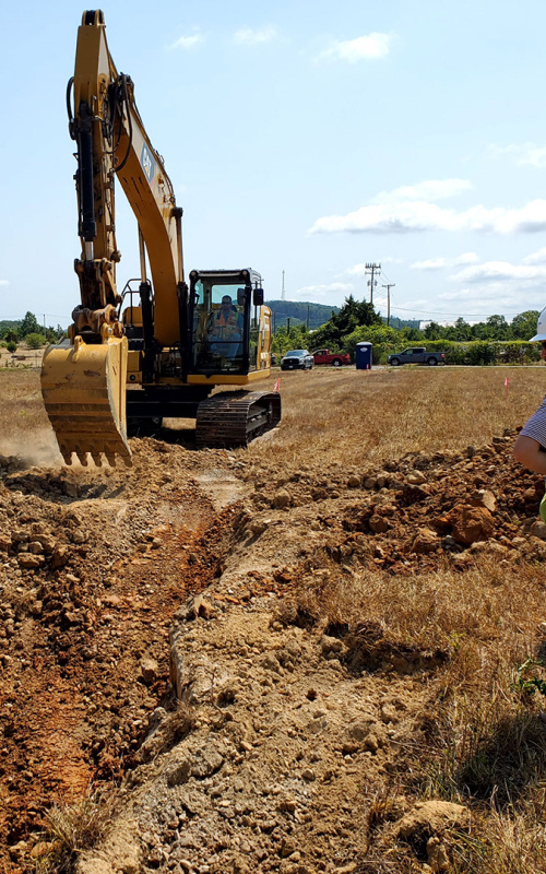 Yellow excavator in field, three people in hard hats watch