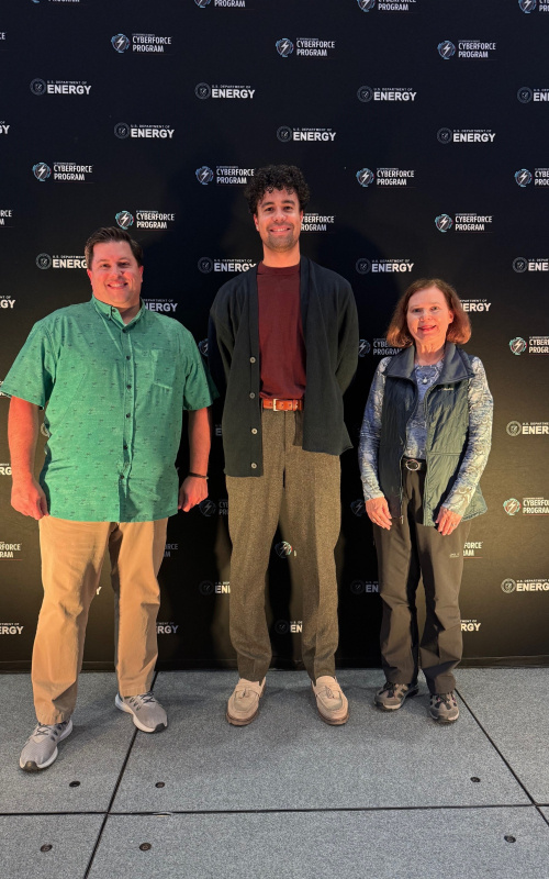 Three people stand against a backdrop of a wall of CyberForce branding.