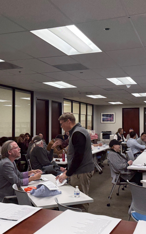A room full of professionals, some sitting at tables and some standing in a room
