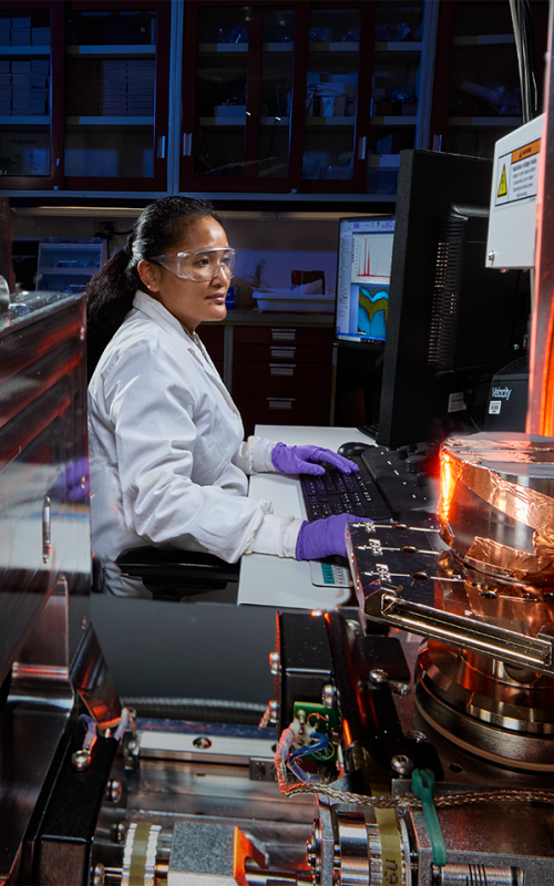 Scientist operates advanced laboratory equipment while monitoring data on a computer. 