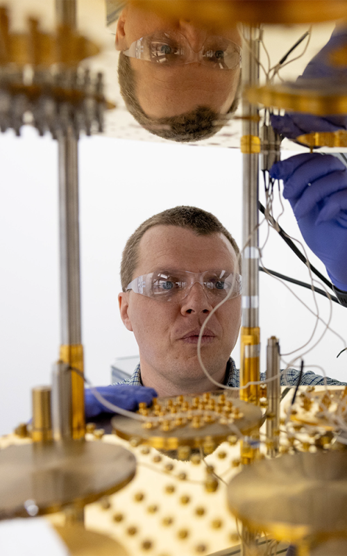 Researcher wearing safety glasses and gloves works with components of a quantum computing system. 