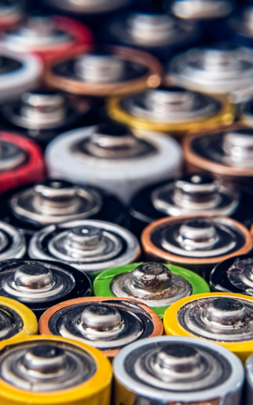 Close-up photo of the positive terminals of many batteries in different colors and sizes.