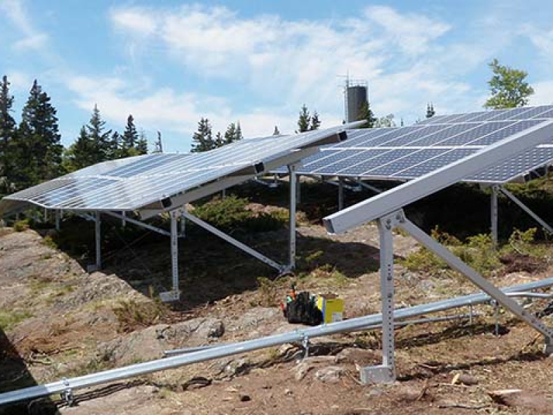 Two rows of solar panels on the side of a rocky hill.