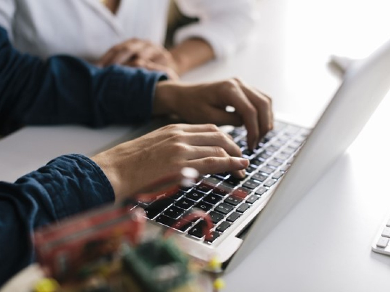 two people at a table with an open laptop and one person's hands on the keyboard.