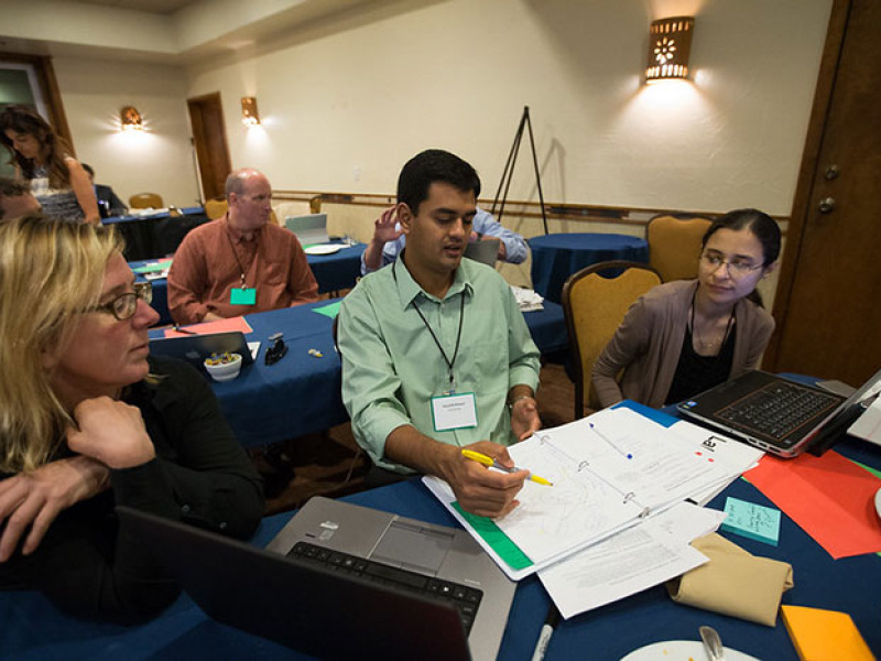 A team of two women and a male work on a project together at a table covered with papers and laptop computers.