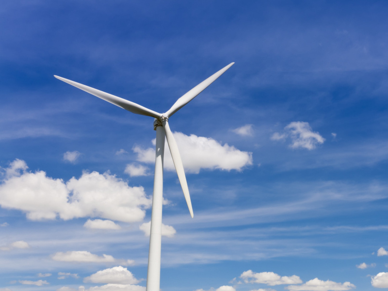 Wind turbine against a sunny sky with clouds.