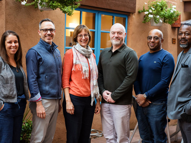 A group of six people stand together for a photo on an outdoor patio.