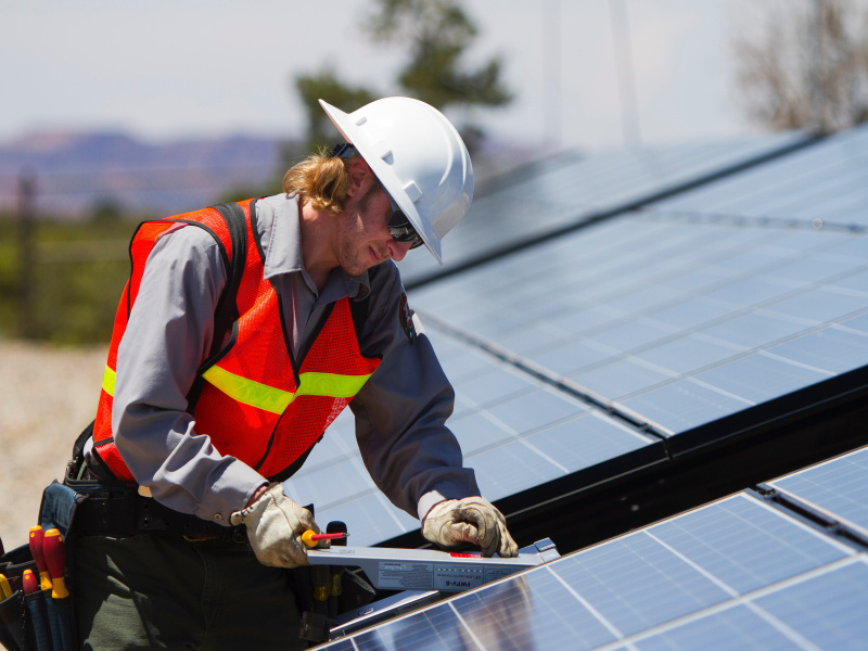 Photo of a man in an orange vest and hard hat performing maintenance on a PV array.