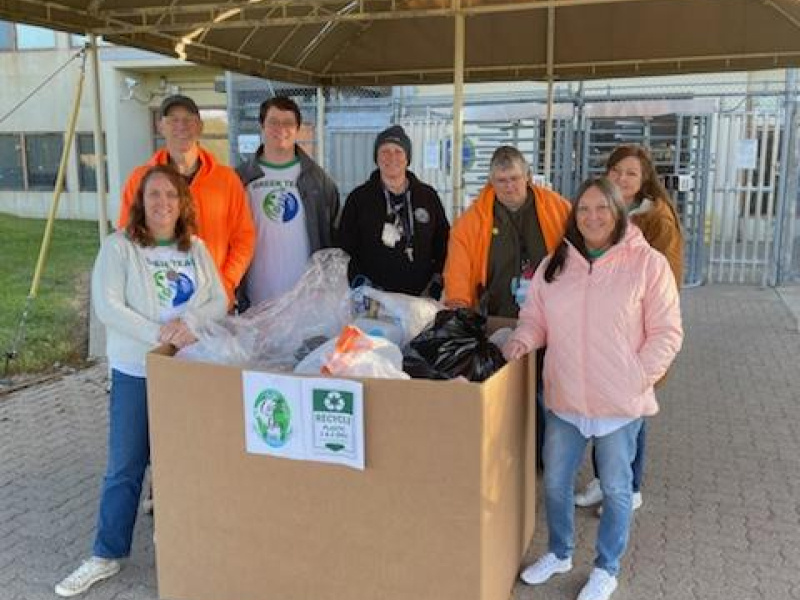 A group of people standing in front of a filled recycling box. 