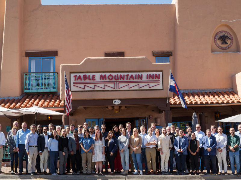 A group of 50 people stand outside in front of a building, smiling for the camera. 