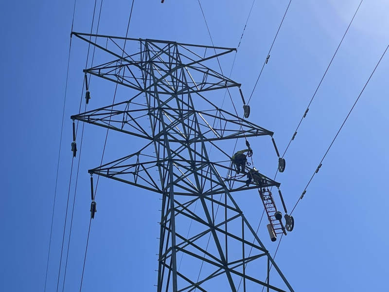 helicopter over transmission tower and lines. blue sky in background.