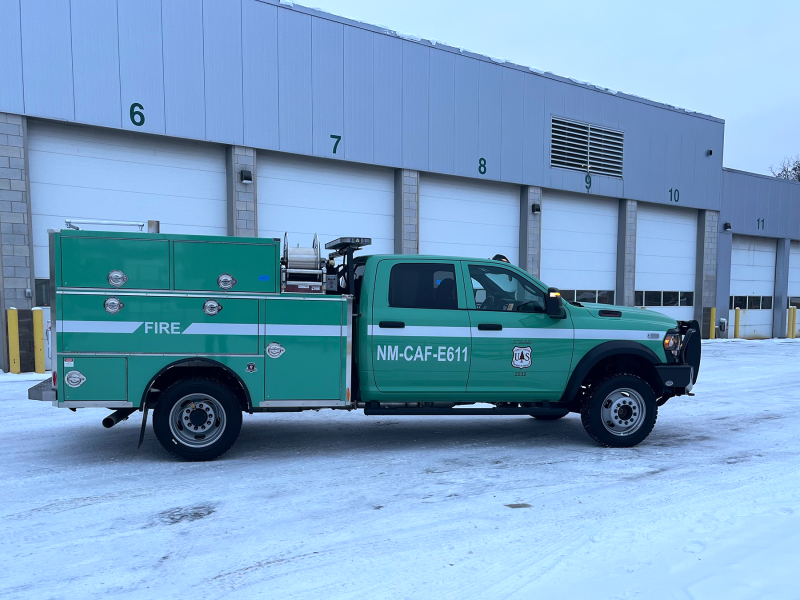 A green federal fleet truck in front of a garage building with multiple bays.
