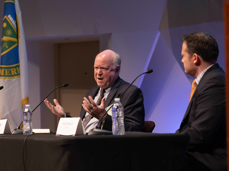 Two individuals sitting at a table speaking into microphones.