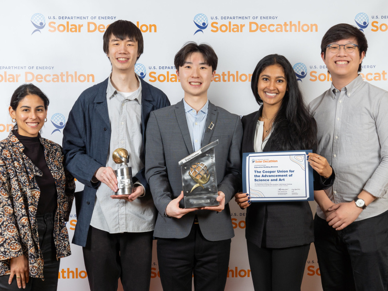 A group of five students from a 2023 Design Challenge team standing together facing the camera, with three of them holding awards.