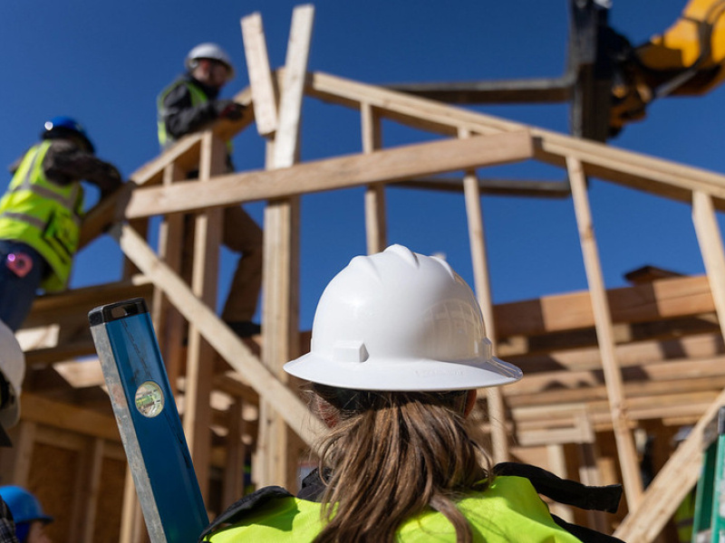 The construction site of a team's Build Challenge house, showing team members in construction attire working on the wood framework of the house.