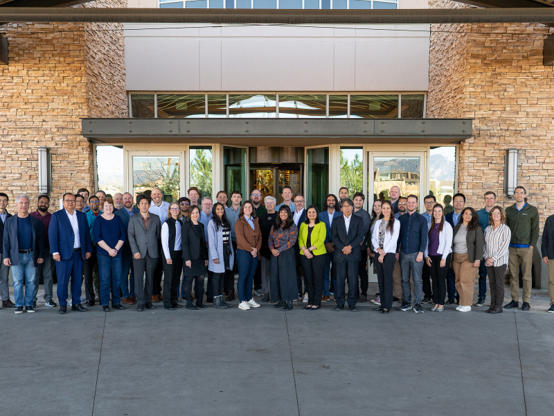 A group of approximately 45 people stand together in front of a hotel lobby. 