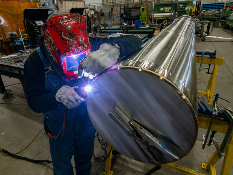 A person welding a large metal cylinder. 