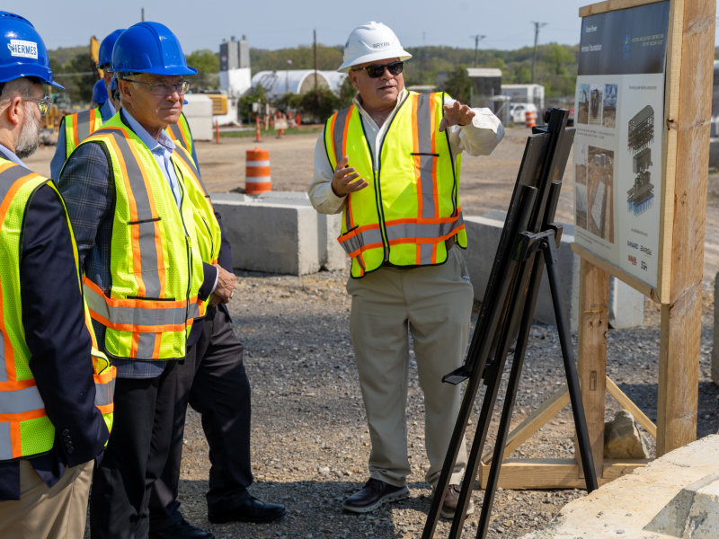 Men in safety vests and hard hats tour the outside of the Oak Ridge site