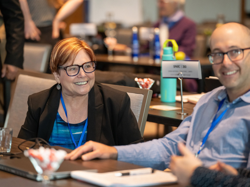 Woman and man listen to others speaking at conference
