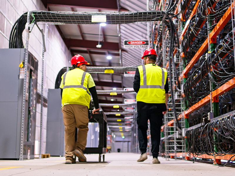 Two technicians wearing PPE walking past racks of equipment in a data center