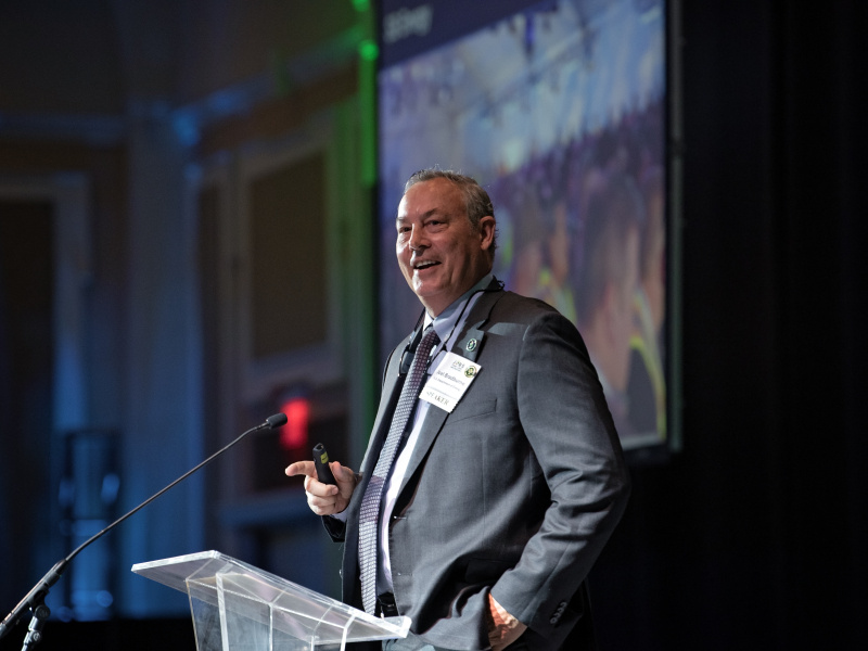 A man in a suit giving a key note address at a conference standing behind a podium