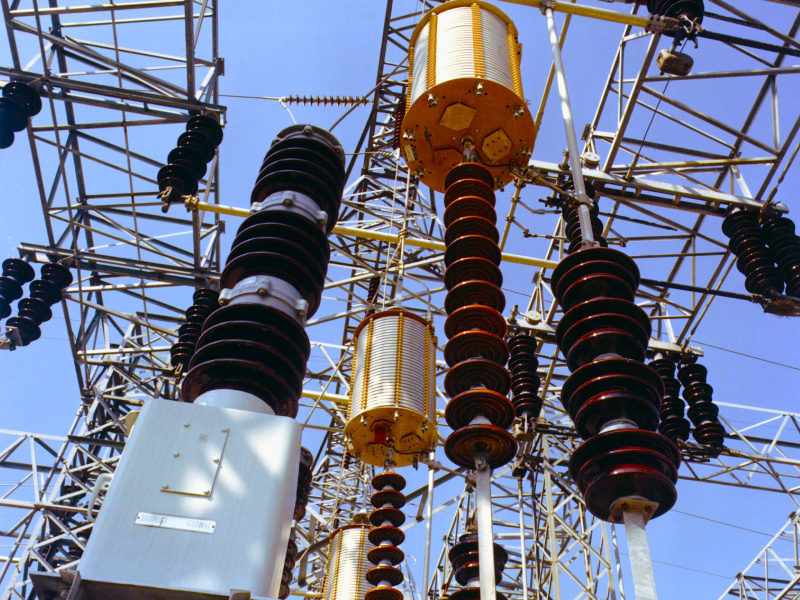 Electrical substation with high-voltage transformers, insulators, and switchgear connected by overhead transmission equipment.