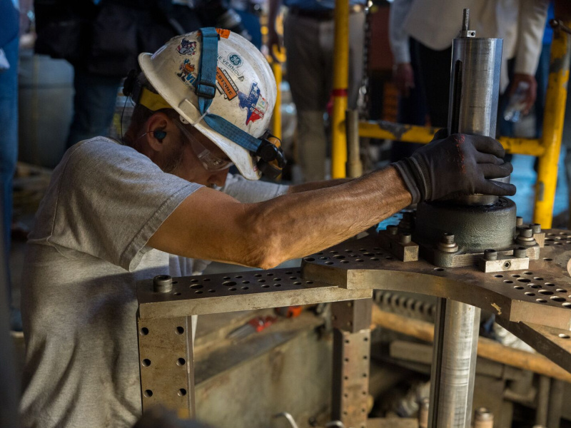 Power plant worker wearing a hard hat, safety glasses, and gloves works on large industrial equipment at the San Juan Power Plant.