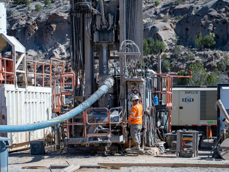 Crews in protective gear working on a large outdoor well at the Los Alamos site with a large blue tube coming out of it