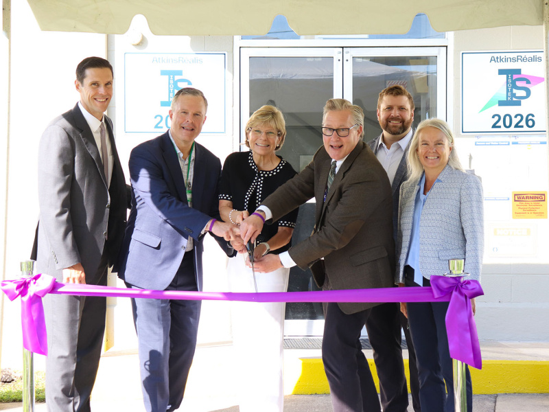 A group of professionals conducting a ribbon cutting in front of a building with a purple ribbon tied in front of them