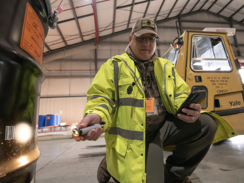 A man in a yellow jacket using a barcode scanner on the side of a black container