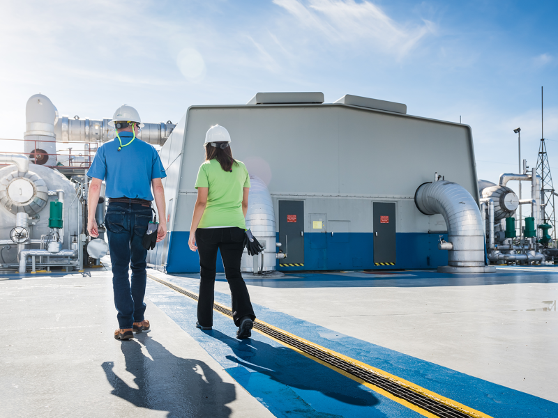 Two workers wearing hard hats walk past the steam turbine building at Robinson Nuclear Plant.