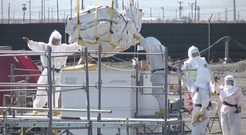 Workers at the Plutonium Finishing Plant guide a large sack containing radioactive waste into a metal container suitable for shipping and storage.