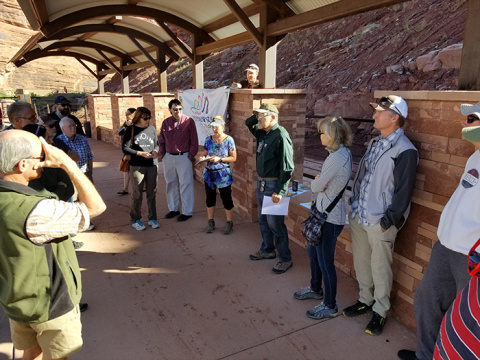 Tour attendees gather around Moab Festival of Science volunteer Lee Shenton, at center, wearing a green shirt and cap.