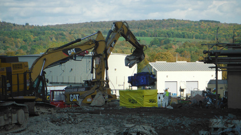 A worker uses an excavator to lower a dust collector into a waste box for shipment to an offsite disposal facility.