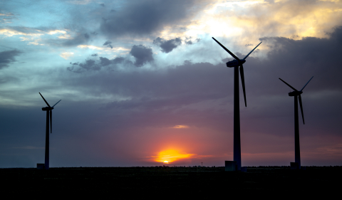 Photo of three wind turbines taken with the sun setting behind them.