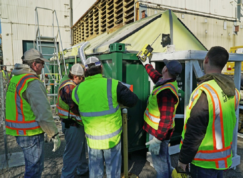 Employees with EM cleanup contractor UCOR install fogging equipment on a debris container at the Oak Ridge Site.