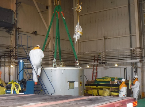 Workers use a 100-ton crane to lift a waste container and its interior concrete shield onto a flatbed trailer. They also placed the container’s exterior steel shield on the trailer.