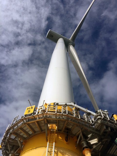 View of an offshore wind turbine from underneath against a cloudy sky.