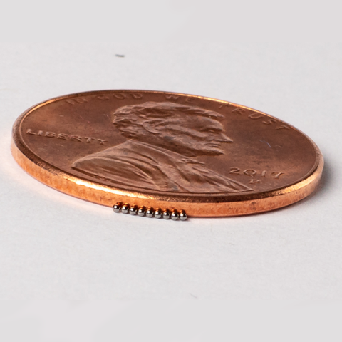 Closeup photo of a penny next to MiniFuel targets that look like tiny beads, to show scale.