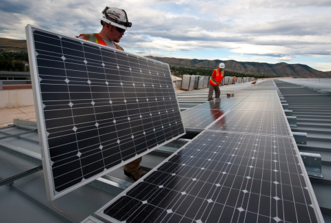 three men carry or install solar panels on a rooftop.