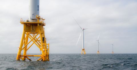 Photo of 4 wind turbines on orange platforms in the middle of ocean.
