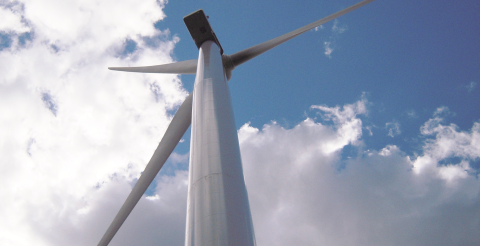 View from below of a wind turbine against a blue sky with some clouds.