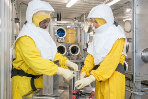 Savannah River Site radiation protection employees don protective equipment while working in a glovebox. Gloveboxes are structures with ports containing gloves that allow waste handlers to safely work with radioactive material.