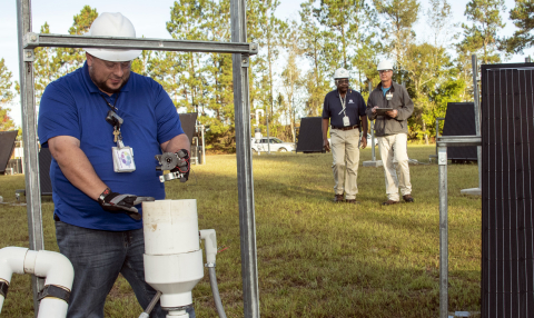 Savannah River Nuclear Solutions (SRNS) Mechanic Thad Ashely, foreground, checks components of a soil vapor extraction unit, as SRNS engineers Joao Cardoso-Neto, background, left, and John Bradley inspect solar panels.