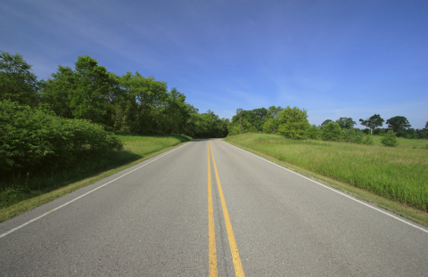 A two-lane road with grass and trees on each side, from the perspective of the center line of the road.