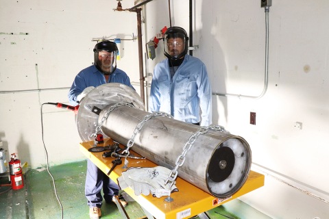 Isotek employees Shane Miles, left, and Ryan Souza stand behind a cutting tool used to help install new remote manipulators in hot cells at Oak Ridge.