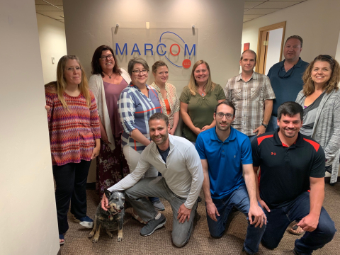 In this photo from February, MarCom employees are shown with the company’s mascot, the dog Moxie. MarCom President Marcella Medor is second from left. 